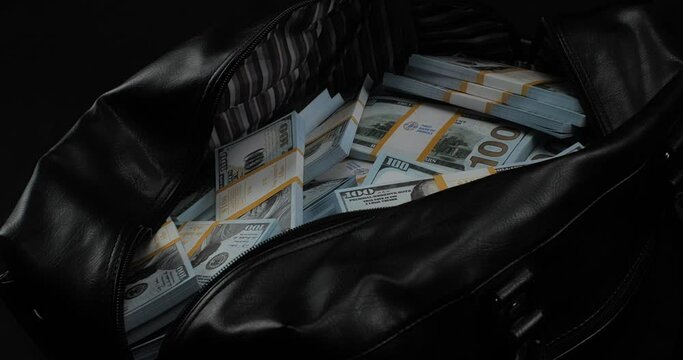 Close-up of a large bag full of money one hundred dollar bills. A bag full of packs of one hundred dollar bills stands on a black background. The concept of wealth, a lot of money.