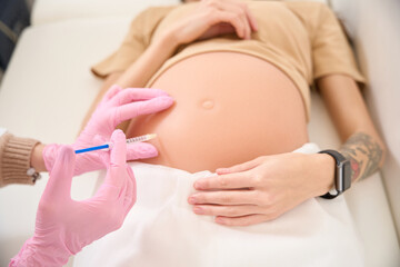 Cropped of gynecologist doing injection with syringe in pregnant belly of woman