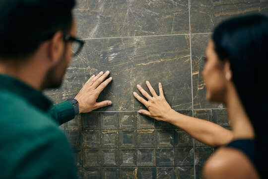 A couple searching for the right ceramic tile for their bathroom, touching one with their hands.