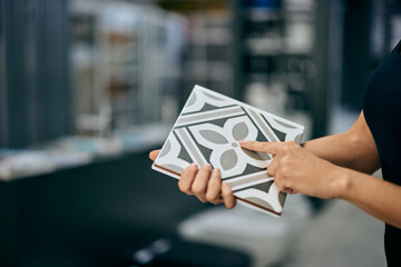 Female hands holding a ceramic tile, looking at the design on it, at the home design shop.