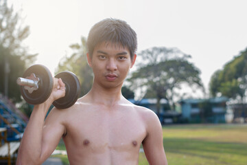 Asian preteen boy lifting dumbbells to loose weight and to do the bodybuild in grass field in late...