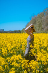 Fototapeta premium Brunette girl standing in blooming yellow field, enjoying natural beauty, plant material production, flower bloom and scent for perfume making.