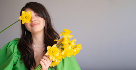 Woman covers eye with daffodil, smiles at camera. Happy recipient of Mother's Day bouquet. Spring...