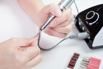 A girl gives herself a manicure using a nail drill