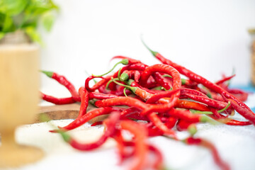A wooden table has a pile of red chili peppers on it. The peppers are different shades of red and different lengths. There is a white background.
