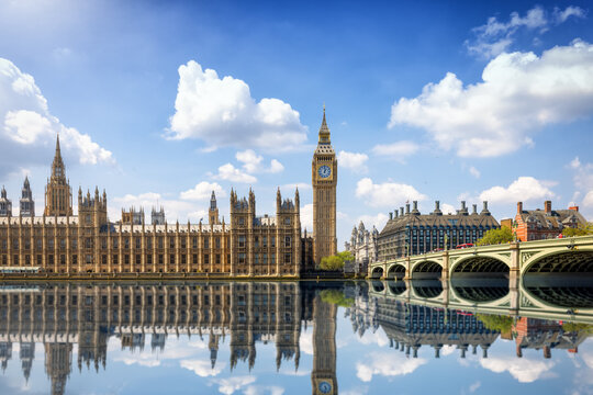 Summer view of the Westminster Bridge and Palace with Big Ben clocktower in London, England, with sun, clouds and reflections in the river Thames