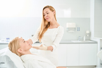 Fototapeta premium Cosmetician looking at client face after bio revitalization procedure