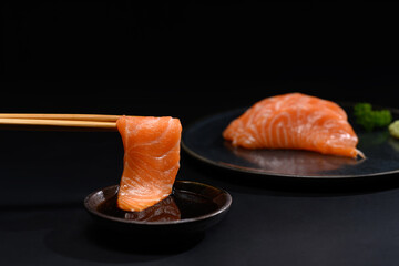 Closeup chopsticks with fresh salmon sashimi dipping into soy sauce. Japanese food style