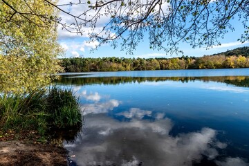 vue sur le lac d'Aydat dans le puy de dôme avec ses eau bleue et ses reflets d'arbre et de nuages entourée de forets