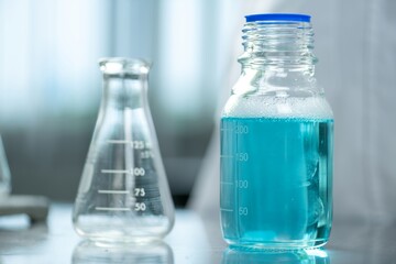 Blue liquid in a glass bottle and an empty beaker on a lab table.