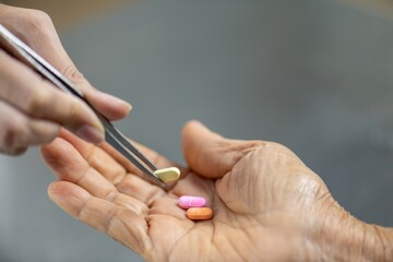 A hand holding a pair of tweezers is picking up a pill from an open palm.