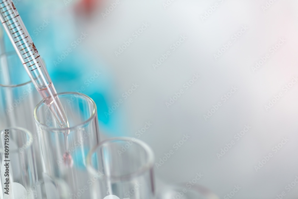 Wall mural a close up of a pipette adding a red liquid to a test tube in a laboratory with a blurred background
