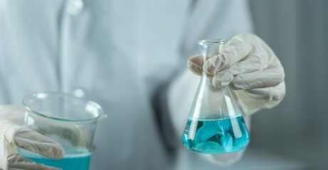 A gloved hand holding up a nearly full flask of blue liquid.
