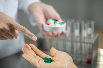 A pharmacist is holding a pill in their hand and pointing to it with their other hand.