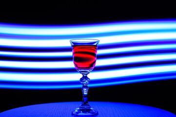 Efektowny kryształowy kieliszek na wino postawiony na tle smug światła w niebieskim kolorze 