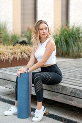 Positive young caucasian woman holding yoga mat after workout. Blonde girl wearing top and leggings...