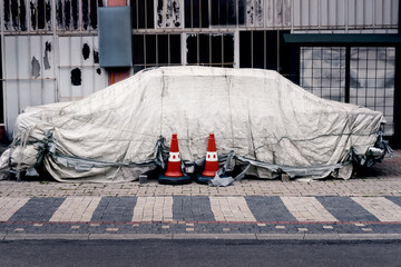 Broken abandoned car in parking covered with protective cover, old car on city street wrapped in...