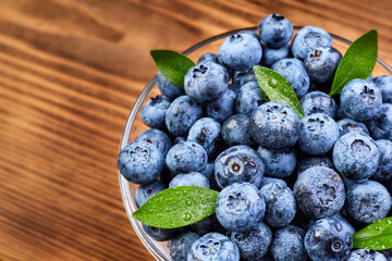 Blueberries with green leaves in a glass plate and water drops on a wooden background
