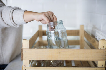A woman wants to send washed glass jars for recycling and puts them in a drawer in the kitchen. An...