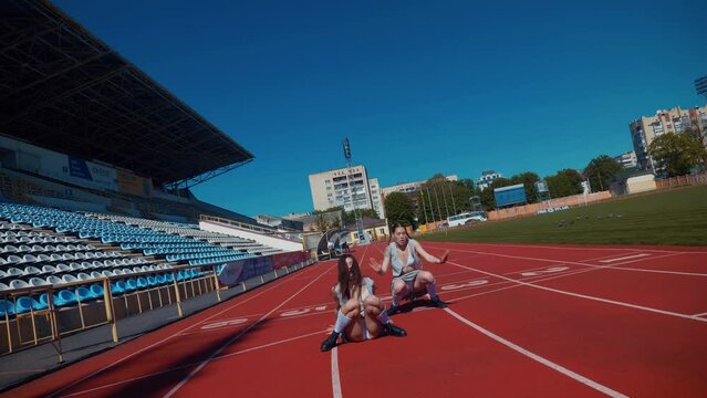 Two fiery women joyfully dancing on a stadium track. Women cheerleaders in short skirts happily dancing on the running track. Two girls in bras seductively dancing together on a sports track. Women en