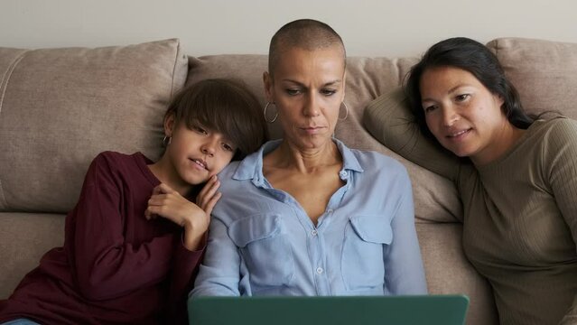 Lesbian couple and a non-binary kid using a laptop sitting on the sofa