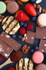 Macarons, chocolate, cookies, berries and various nuts on dark blue background. Top view.