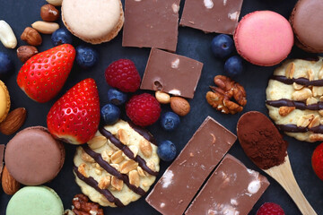 Macarons, chocolate, cookies, berries and various nuts on dark blue background. Top view.