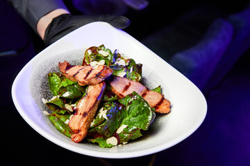 Waiter holding a plate with salad of duck breast and dried cranberry