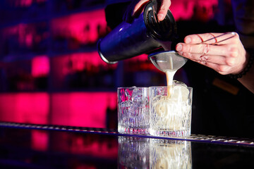 The bartender prepares cocktails on the bar counter using a shaker and a strainer