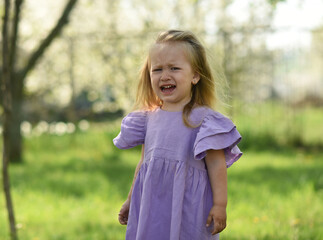 A little girl of two years old is walking in the park. The child is crying and upset
