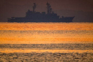 朝焼けが波間に映える海で沖に護衛艦の船影20220604-2