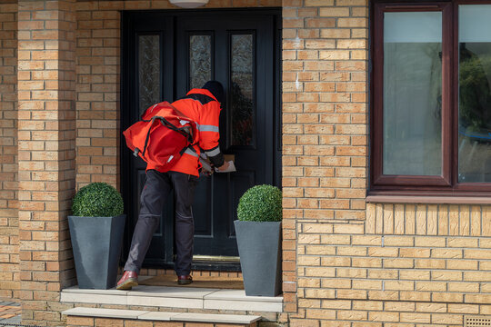 Postman or Mailman in UK posting mail through the letter or mailbox of a house front door