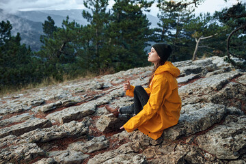 Woman in a yellow raincoat enjoying the serene beauty of nature, sitting on a rock in front of a...