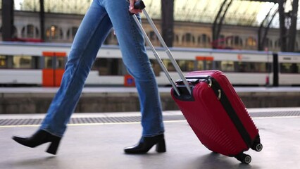 Young traveler woman with travel suitcase walking at train station platform before departure. Travel and vacation concept.