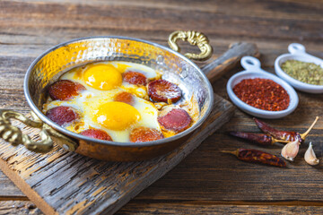 Turkish sausage and eggs fried in copper pan, wooden background, close-up.