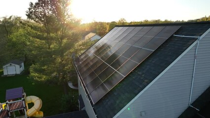 Solar panels on sloped shingle roof of American family home. Aerial slow orbit during golden hour sunset revealing play set in backyard.