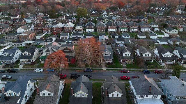 American neighborhood in autumn. Quaint northeastern town with old houses in grid layout. Aerial descending shot revealing trees at dusk.