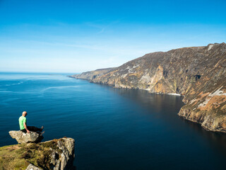 Man enjoys amazing view on Slieve league cliff standing on a edge of a rock. Travel and tourism...