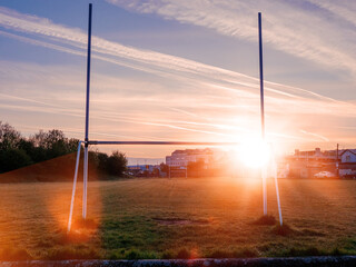 Tall goal post in a field at sun rise. Cloudy sky with sun flare. Irish sport training ground in a...