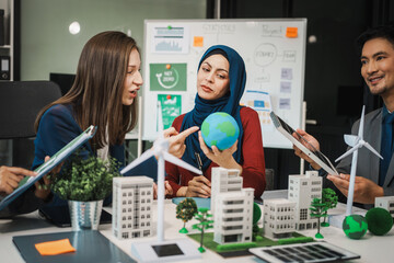 Diverse team, middle-aged Asian businessman, Caucasian young businesswoman, Muslim hijab-wearing businesswoman, meets in boardroom to discuss a wind turbine project for sustainable energy solutions.