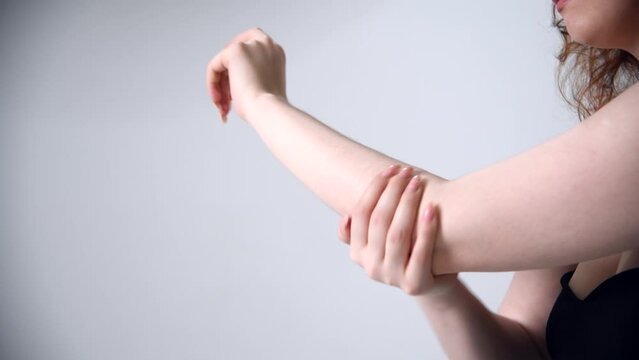 Close-up view of woman rubbing her elbow against grey background. Real time handheld video. Soft focus. Healthcare, cosmetics and self massage theme.