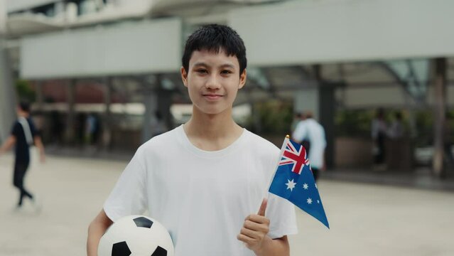 Portrait of the Australian Football Fan Standing Outside, Before the Match Holding the Ball and the Flag. Handsome Positive Boy Looking at Camera with Flag of Australia. Football and People Concept