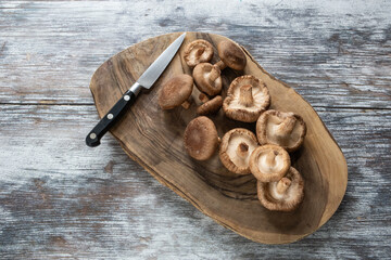 Raw shiitake mushrooms on a wooden board with a kitchen knife