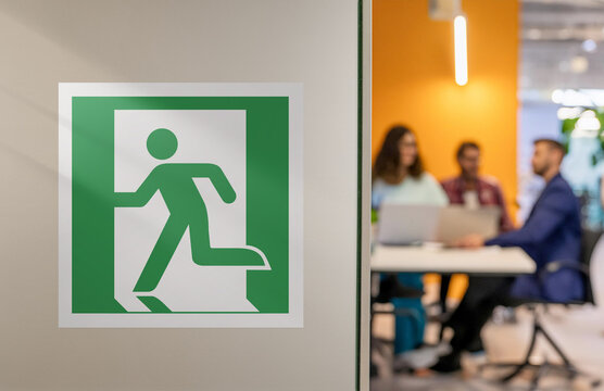 Emergency exit sign on the left on the wall. In the background, interior room of a modern office, industrial premises, laboratories or institutions. Escape and emergency concept.