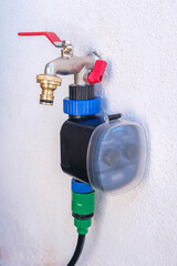 A garden faucet with double water outlet attached to a white wall with an automatic irrigation programmer.