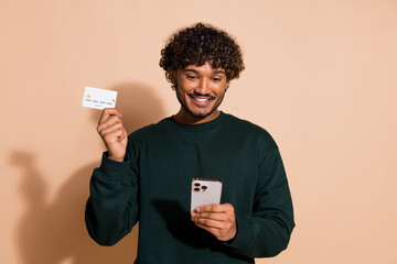 Photo of cheerful positive guy dressed sweatshirt holding bank card communicating device isolated...