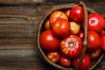 Basket of fresh tomatoes on wooden table, top view.