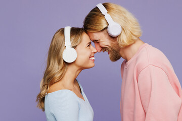 Young couple two friends family man woman wear pink blue casual clothes together listen music in headphones touch each other forehead isolated on pastel plain light purple background studio portrait.