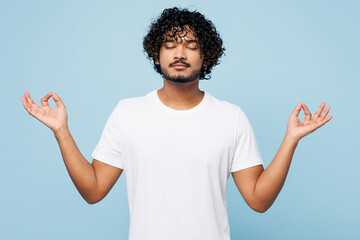 Young Indian man wear white t-shirt casual clothes hold spreading hands in yoga om aum gesture relax meditate try to calm down isolated on plain pastel light blue cyan background. Lifestyle concept.