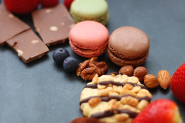 Macarons, chocolate, cookies, berries and various nuts on dark blue background. Selective focus.